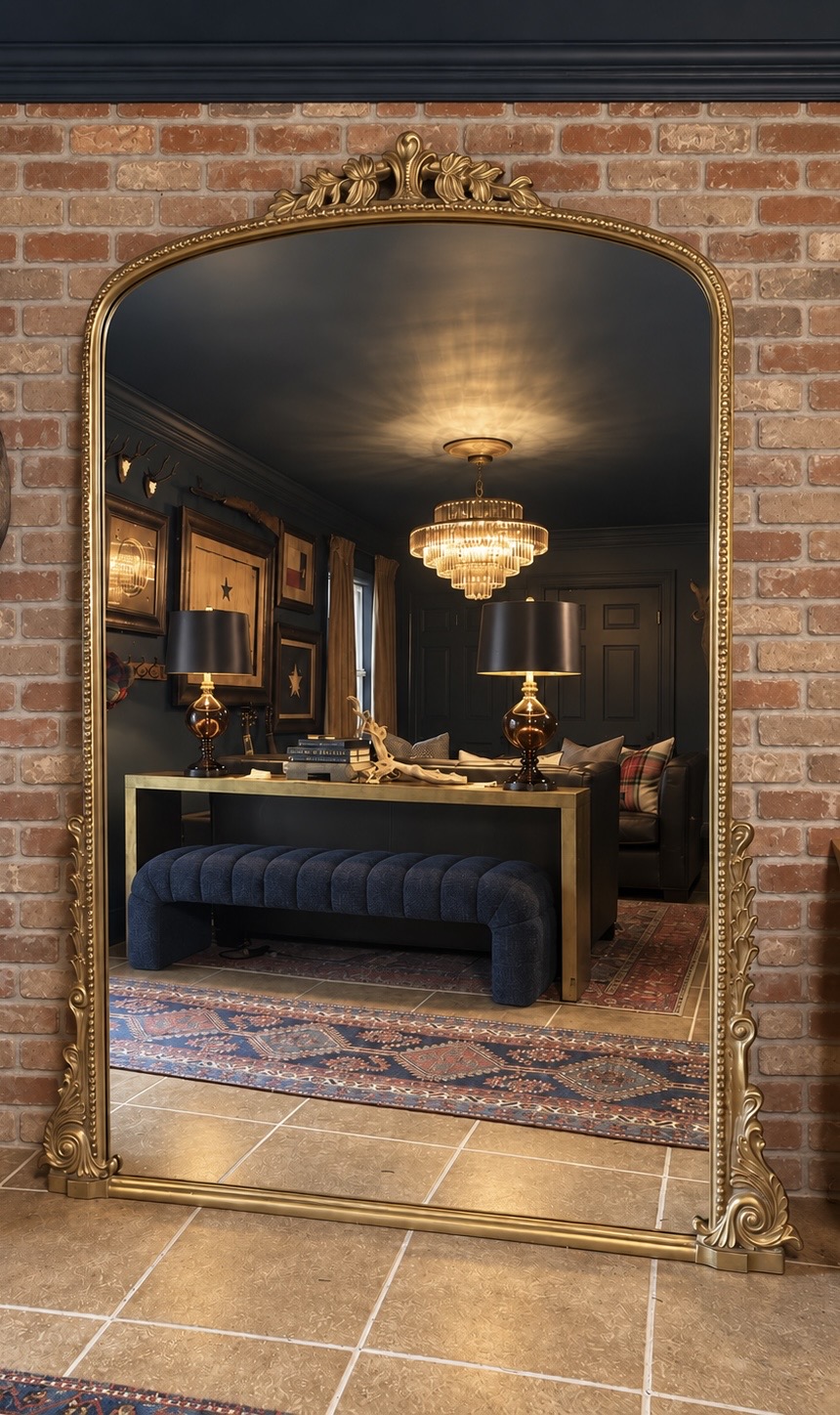 Ornate brass floor mirror reflecting a richly layered dark interior with warm lighting